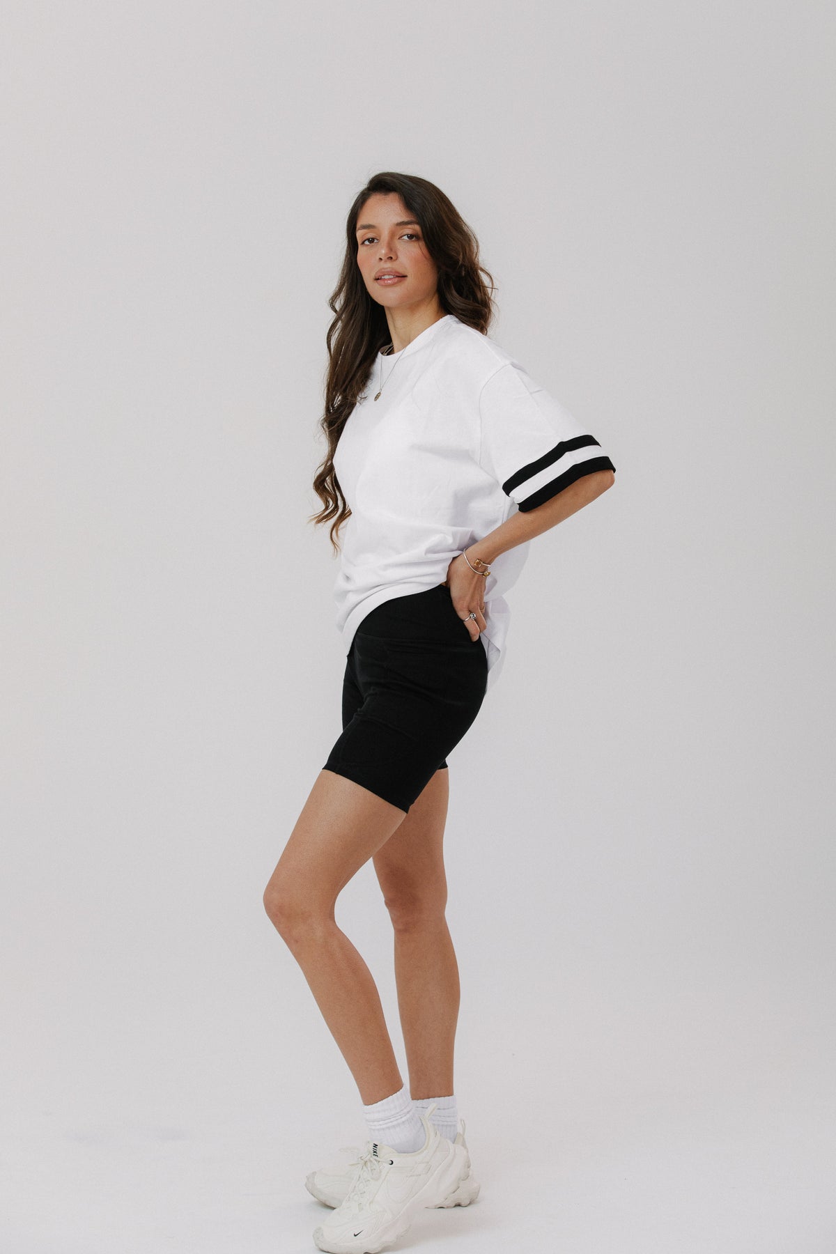 Active women wearing a white oversized 100% cotton t-shirt and black bike shorts on a grey background