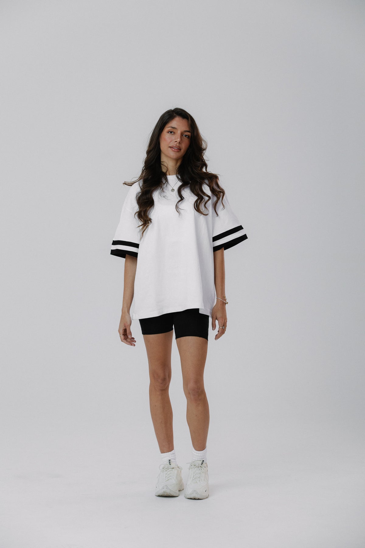 Active women wearing a white oversized 100% cotton t-shirt and black bike shorts on a gray background
