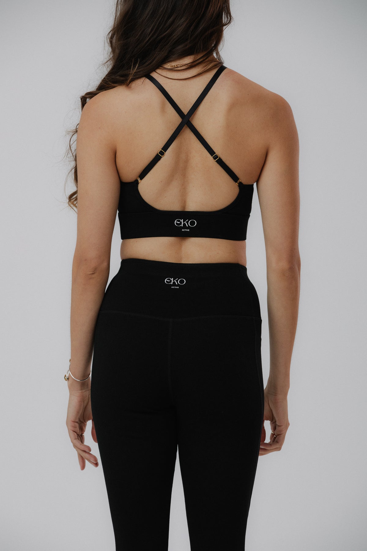 A woman shown from the back wearing a black cotton Eko Active sports bra with crisscross straps and matching black leggings.