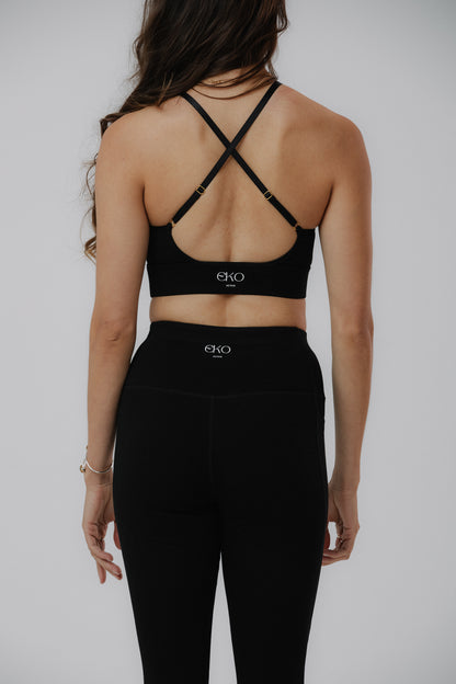 A woman shown from the back wearing a black cotton Eko Active sports bra with crisscross straps and matching black leggings.