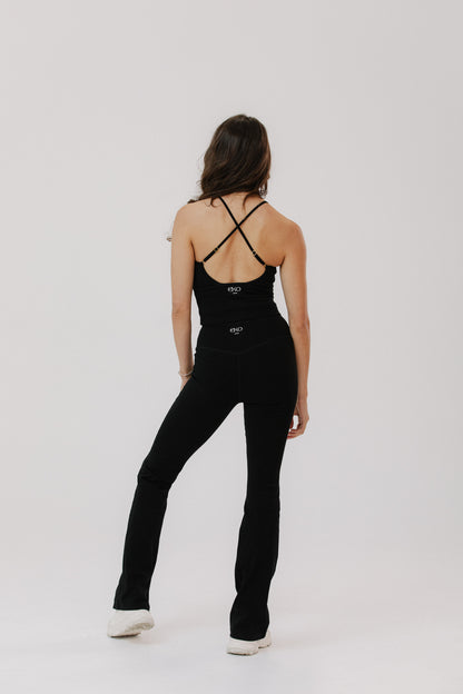 A woman is shown from behind wearing a black strappy cotton tank top and black cotton flared pants.